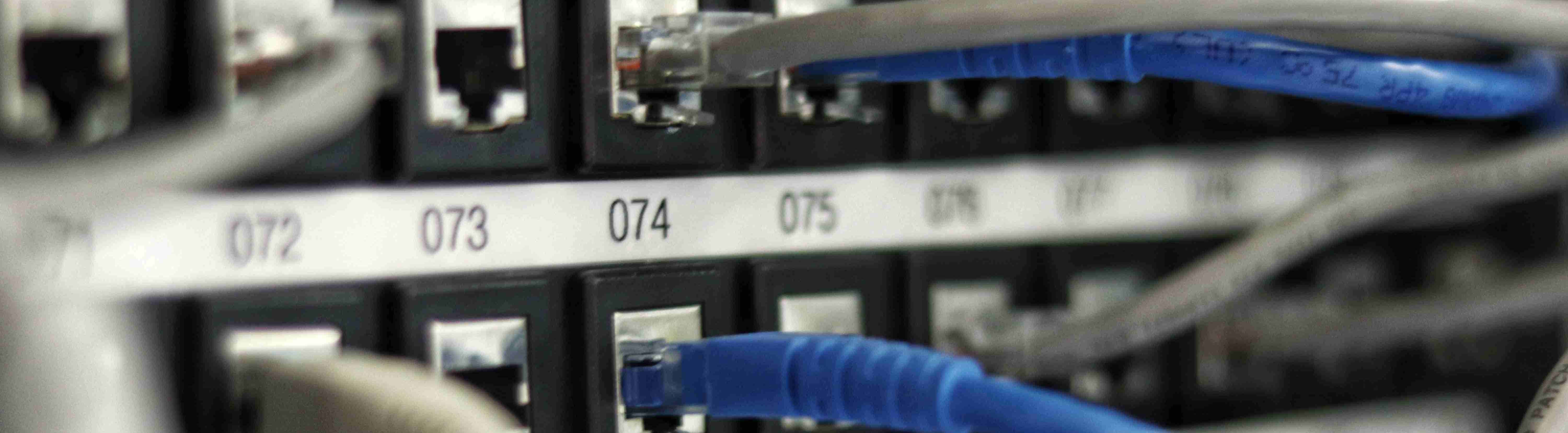 Network patch panel zoomed in on a blue cable plugging into port 074 in between 8 grey cables